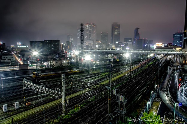 写真: 雨の名古屋高層ビル群の夜景と鉄道の光跡